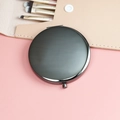 Portable round makeup mirror with elegant black metal frame on a pink background - 70mm / Gunmetal