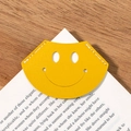 Bright yellow leather smiley face corner bookmark on book page with wood background - Yellow