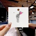 Close-up of a skull hand holding a pink heart lollipop enamel pin on white card - 129*Skeleton Hand with Lollipop Pin