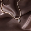 Detail shot of a cream oval pearl necklace with a square zircon pendant on brown silk fabric - Silver Square (Pearl Style)