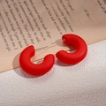 Macro view of matte red C-shaped acrylic hoop earrings on an open book surface - Red Round