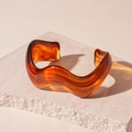 Vista macro del brazalete ondulado de resina ámbar con vetas sobre soporte de piedra - Ámbar