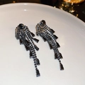 Vue macro d'élégantes boucles d'oreilles noires à pompons et strass sur assiette blanche - Noir de Jais (Tige en Argent Sterling 925)