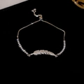Dettaglio del bracciale regolabile con piuma in zirconi e catena a griffe su fondo nero - Stile Piuma / Piuma d'argento