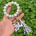 Detail of beaded keychain wristlet with cow print Mama charm and tassel on green background - Grey/Marble Print