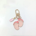 Detail of pink enamel baby feet and milk bottle charms on a golden metal keychain - Style A / Pink