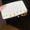 Detailopname van gouden oorbellenset met zirkonia oorknopjes en ringen op sieraadkaart - Oorsluiting - Goud (8-delige Set)