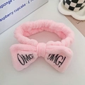 Pink coral fleece headband with black OMG! embroidery on a minimalist white desk setup - Pink