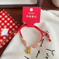 Close-up of red woven bracelet with pink glass beads and a golden pig zodiac pendant - Gold Zodiac Pig Pink & White Beaded Bracelet