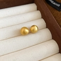 Macro detail of golden brushed metal ball earrings resting in a beige velvet jewelry box - 10mm / Gold