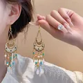 Dettaglio di orecchini boho con nappine, motivo floreale a mezzaluna e perline colorate - Stile Etnico in Smalto Mezzaluna Oro / Bianco