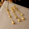 Makroaufnahme von goldenem Tropfen-Schmuckset auf gebürsteter Metalloberfläche mit Glanz - Halskette-Ohrring-Set (Gold) / Gold