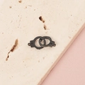 Macro shot of a black metal handcuff pendant on a stone slab with soft pink background - Black