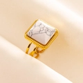 Detailed macro view of a gold-tone stainless steel ring with white marble stone inlay - Gold/White Marble Texture