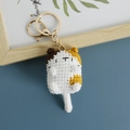 Handmade crochet calico cat keychain with gold metal clasp on a blue surface - Calico Cat
