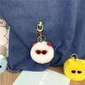 Detail view of cute fuzzy plush ball keychains with sunglasses on denim bag - Purple