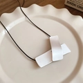 Détail du pendentif géométrique argenté sur cordon noir posé sur une assiette en céramique - Style Rectangulaire Argenté