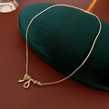 Detalle de un collar con colgante de serpiente dorada sobre un expositor de terciopelo verde - Oro (Chapado En Oro Real)