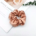 Detail of rose gold satin scrunchie with glossy pleated texture on a white surface - Light Coffee