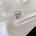 Gros plan de boucles d'oreilles géométriques argentées sur un tissu en soie blanche - Argenté