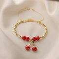 Detail of gold cherry pendant bracelet with red enamel beads on beige satin fabric - Bright Red Beads Cherry Pendant (E000443YS)