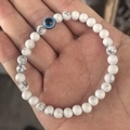 6mm white turquoise beaded bracelet featuring a blue evil eye stone held in hand - White Howlite
