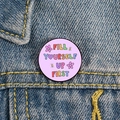 Macro shot of a purple enamel pin with Fill Yourself Up First text on denim jacket - XZ4791-Fill Yourself Up First