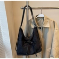 Detalle de bolso tote de ante negro con lazo decorativo junto a una gabardina de color beige - Negro