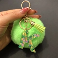 Detail of neon green pompom keychain featuring resin letter K with heart sequins - Letter K