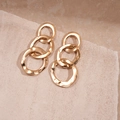 Macro shot of gold triple-interlocked textured ring earrings on a minimalist stone base - Gold