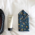 Plano cenital de un pañuelo de algodón floral junto a crema de manos y zapato acolchado - Verde azulado