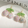 Detail of colorful woven cherry earrings with green leaves on white ceramic plate - Colorful