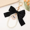 Detail of elegant black bow and pearl keychain with number 5 charm on a soft beige tray - Black