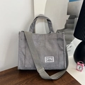 Grey corduroy tote bag with adjustable shoulder strap and large front pocket on wooden table - Gray