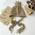 Stijlvolle beige grofgebreide trappermuts met gevlochten kwastjes en oorklappen - Lichtkoffie