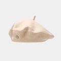 Detailed macro view of beige wool beret featuring a metallic badge and top rope accent - Beige