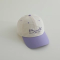 Detalle de gorra infantil bicolor con bordado púrpura sobre tela color crema - Morado