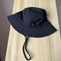 Detalle de sombrero de pescador negro con cordón ajustable sobre fondo de madera clara - Talla única / Negro