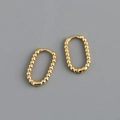 Detail von goldenen U-förmigen ovalen Creolen mit Perlenstruktur auf grauem Grund - 18K Gold
