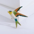 Dettaglio macro della spilla uccello con smalto colorato e cornice dorata su sfondo bianco - Verde