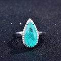 Close-up of a pear-cut Paraiba tourmaline ring with halo setting on a black background - Adjustable Open / Style I-Paraiba Pear Halo