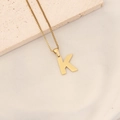 Detailed view of gold letter K pendant necklace with textured surface on a stone background - Letter K