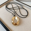 Gros plan d'un pendentif ovale doré minimaliste sur un collier en cordon noir - Pendentif Doré Avec Corde Noire