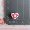 Macro shot of a mini pink resin heart charm with measurement scale on a grid mat - White and Watermelon Red
