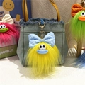Close-up of a yellow plush monster keychain with 3D eyes and bow on a denim bag - Yellow