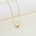 Collana minimalista in oro con ciondolo a sfera cava su un piedistallo bianco - Arancione