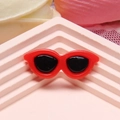 Macro shot of small red heart-shaped resin sunglasses on a pink geometric stand - Red