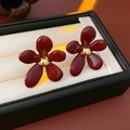 Detail von Vintage-Blumenohrringen in Rot mit goldenem Zentrum auf einem Schmuckkissen - Rot