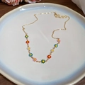 Close-up of golden necklace with colorful enamel daisy pendants on a ceramic tray - Enamel Colorful Daisy Flower Pendant Necklace