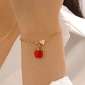 Dettaglio di bracciale dorato con mela in smalto rosso e piccolo ciondolo a cuore - Bracciale Stile Mela (12383)